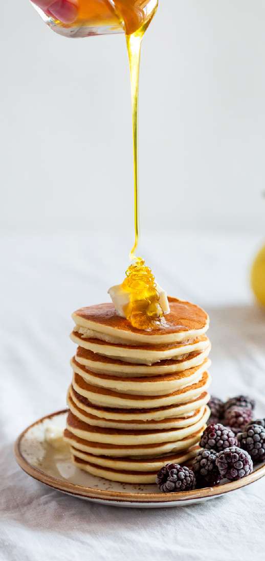 Stack of buttermilk pancakes drizzled with honey and fresh blackberries — luxury inflight breakfast